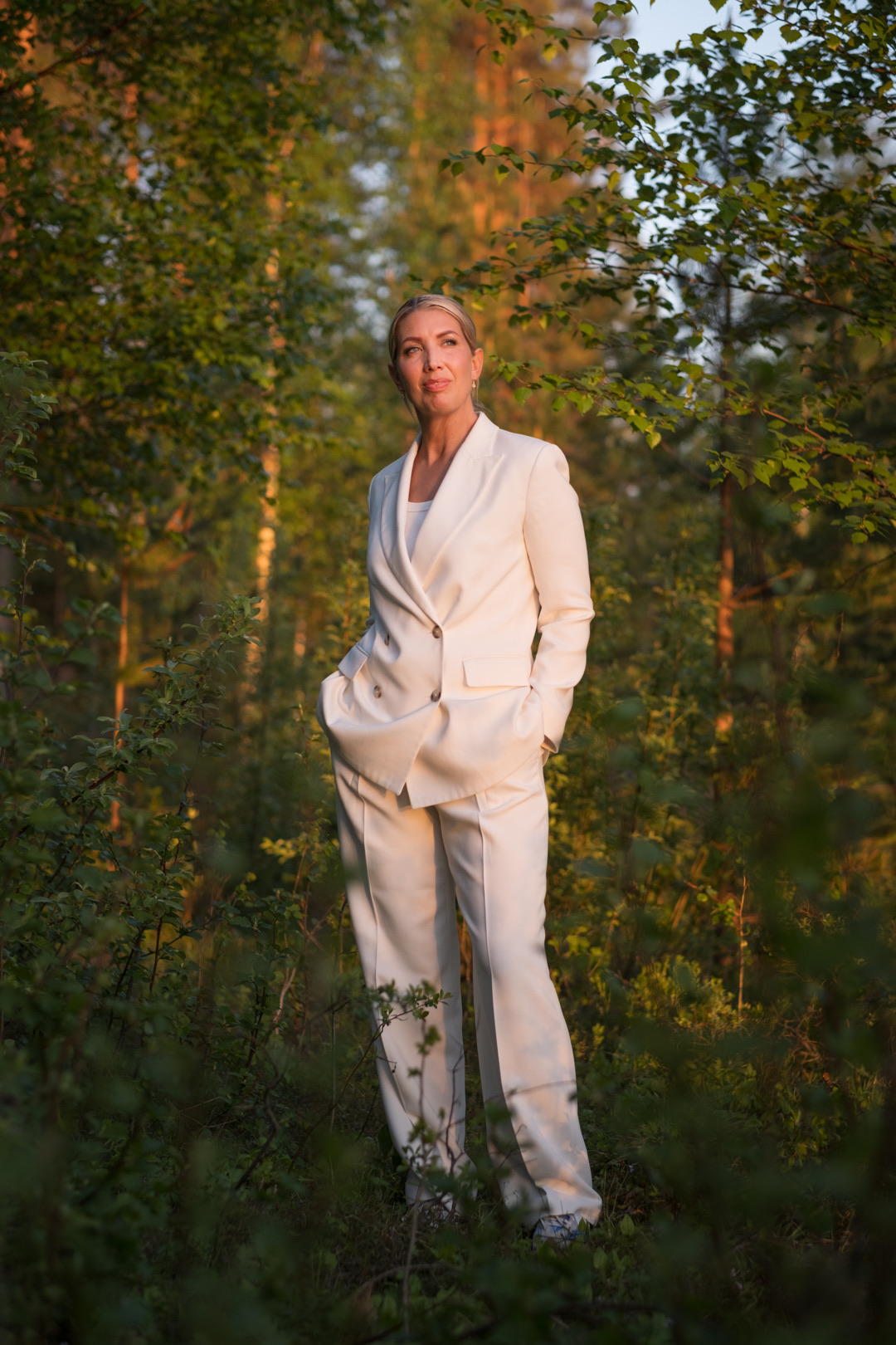 Lina Skandevall i vit kostym i varmt kvällsljus bland träden